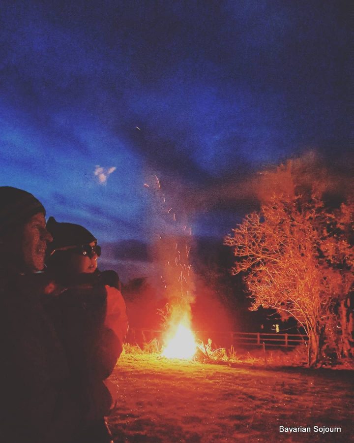 Bonfire night UK, father and young child standing watching fireworks with bonfire in background 