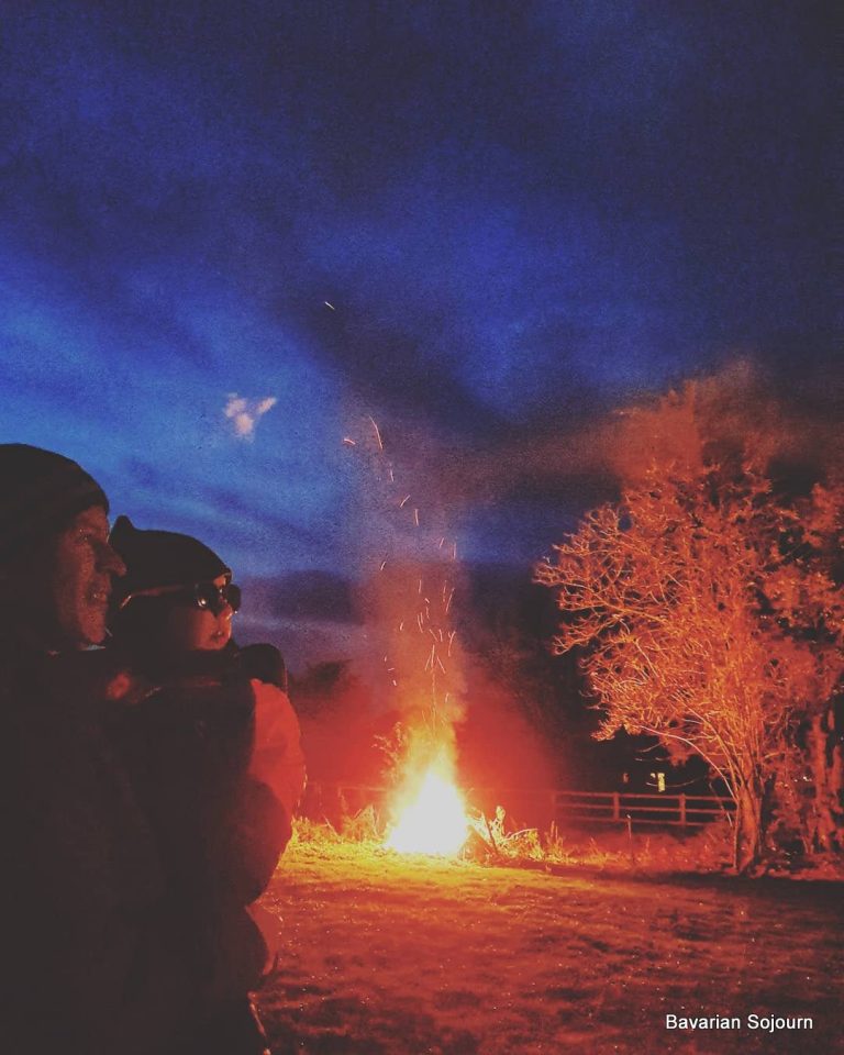 Bonfire night UK, father and young child standing watching fireworks with bonfire in background